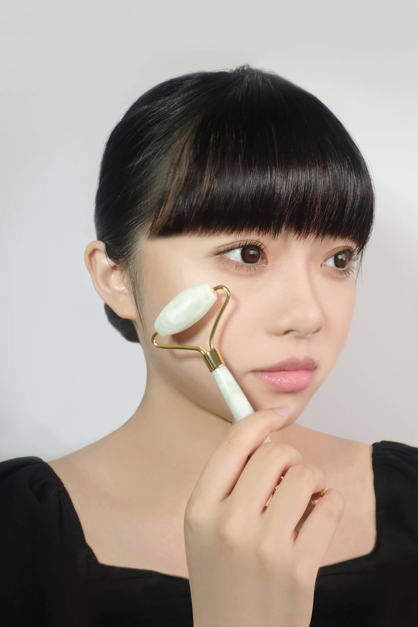 モデルが頬にフェイスシャル クォーツローラーを当てて、顔のむくみとくすみをケアしているシーン。