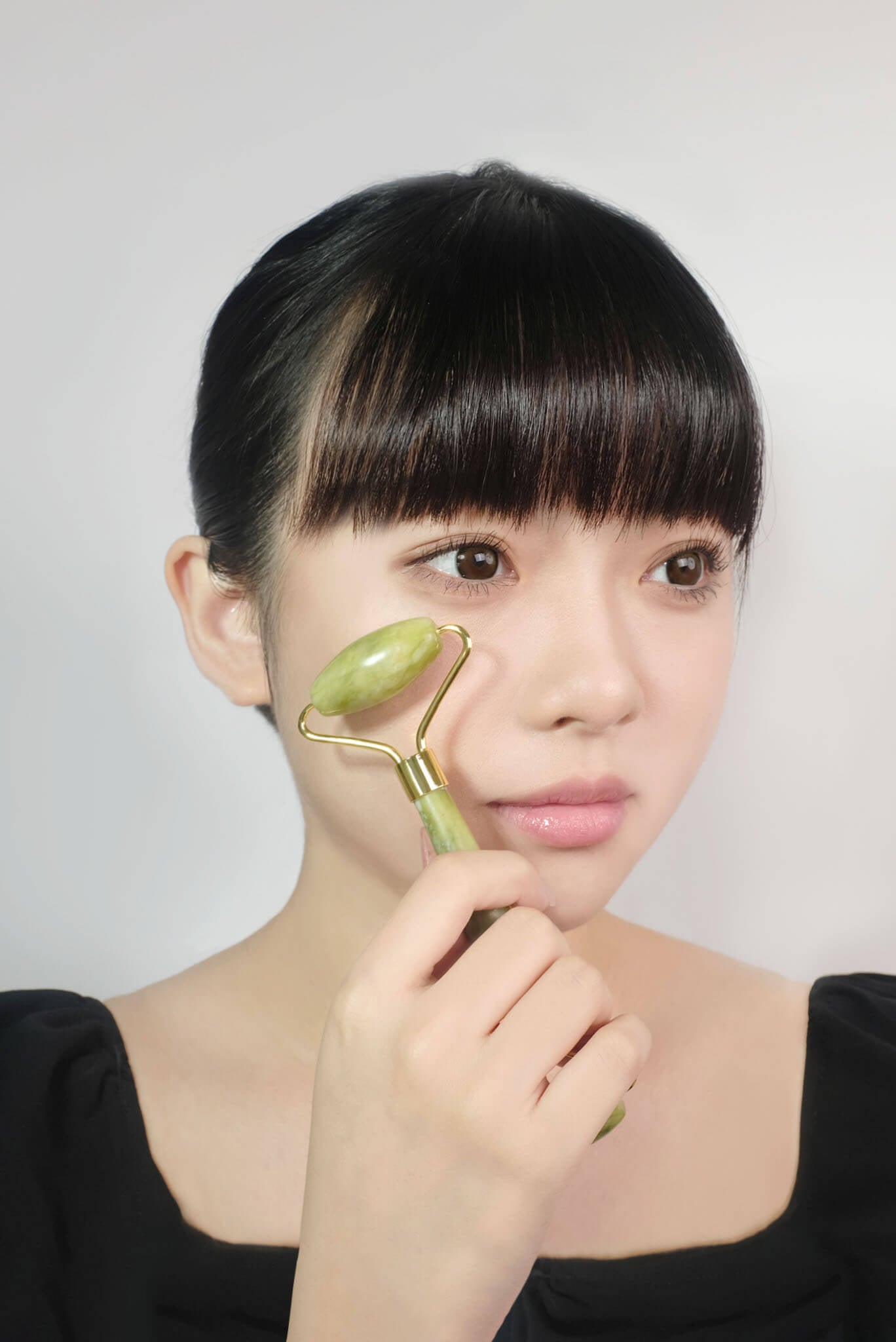 モデルが頬にフェイスシャル ジェイドローラーを当てて、顔のむくみやクマをケアしているマッサージシーン。