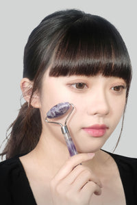 モデルが頬にフェイスシャル ローラー パープルクォーツを当てて、冷感ケアとフェイスリフトマッサージをしているシーン。